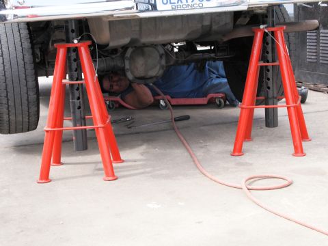 1994 Ford Bronco - Mechanic works on the underside of a 1994 Ford Bronco, which is supported by red jack stands.