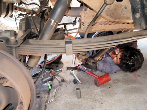 1994 Ford Bronco - A mechanic works on the rear suspension of a vehicle, surrounded by tools on the garage floor.