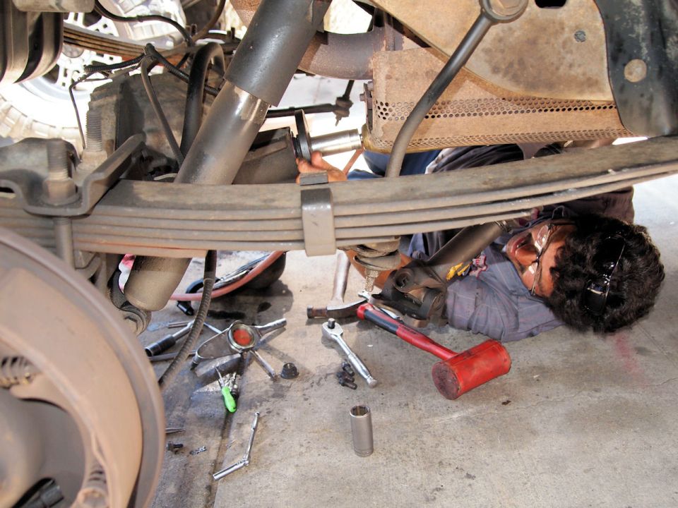 Mechanic lying on floor working on rear suspension of vehicle. Tools scattered around