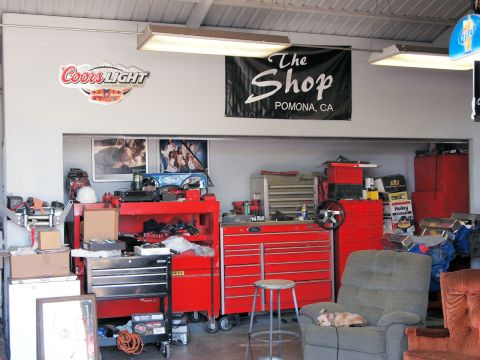 1994 Ford Bronco - A cluttered garage scene shows tool chests, a dog resting, and shop memorabilia on the wall.
