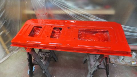 1983 Ford Bronco - A bright red tailgate is shown during a painting process, supported by sawhorses in a workshop setting.