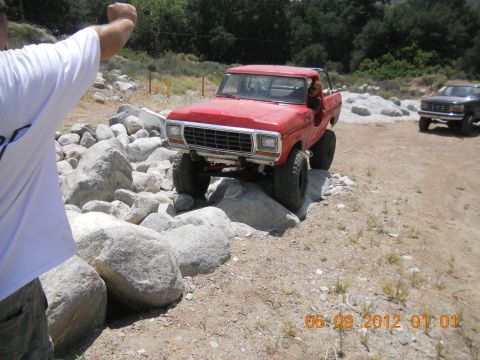 1986 Ford Bronco - A red 1979 Ford F-150 pickup truck is shown off-roading over large rocks, with another vehicle visible in the background.