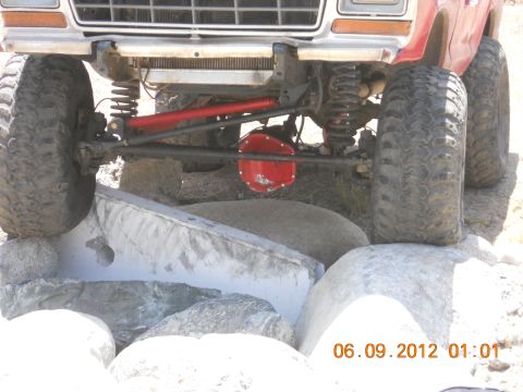 1986 Ford Bronco - This modified truck is shown with its front wheels positioned on large rocks, highlighting its off-road capabilities.