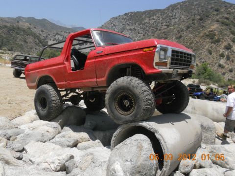 1986 Ford Bronco - Modified red Ford Bronco navigating a rocky obstacle course with other vehicles present.