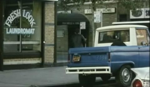 1976 Ford Bronco - Rear view of a blue 1976 Ford Bronco pickup truck parked on a street next to a laundromat.