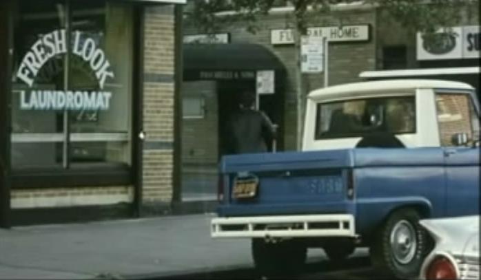 Blue 1976 Ford Bronco pickup truck parked on street, laundromat sign visible