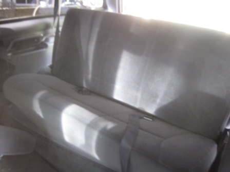 1993 Ford Bronco - The interior of a vehicle shows the rear bench seat and seatbelts, with sunlight streaming in.
