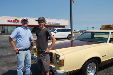 1975 Ford Ranchero - A cream and brown 1977 Ford Ranchero is parked in front of a strip mall, with two men standing beside it.