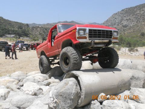1986 Ford Bronco - Modified red Ford Bronco navigating an obstacle course with other vehicles present.