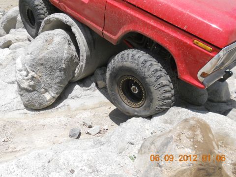1986 Ford Bronco - A red off-road vehicle navigates a challenging course of rocks and a concrete pipe, as seen on SuperMotors.net.