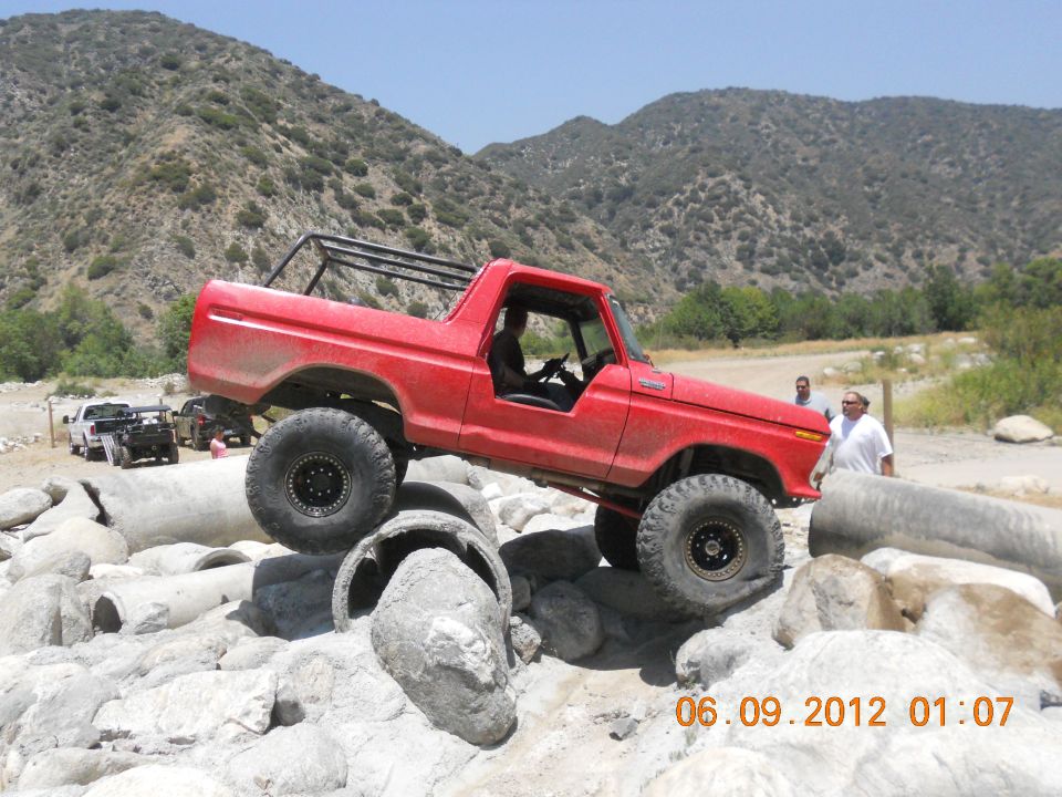 Red Bronco climbing over rocks, another truck in background
