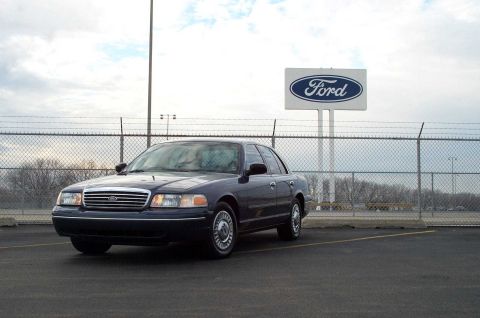 1998 Ford Crown Victoria - A 1998 Ford Crown Victoria is parked in a lot under a large Ford sign.