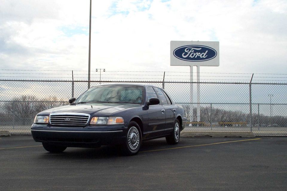 Dark blue Ford Crown Victoria sedan parked in front of a Ford sign and fence