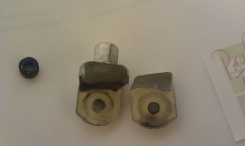 1965 Ford Mustang - Two metal brackets and a small bearing are shown on a white surface, possibly for automotive repair or replacement.
