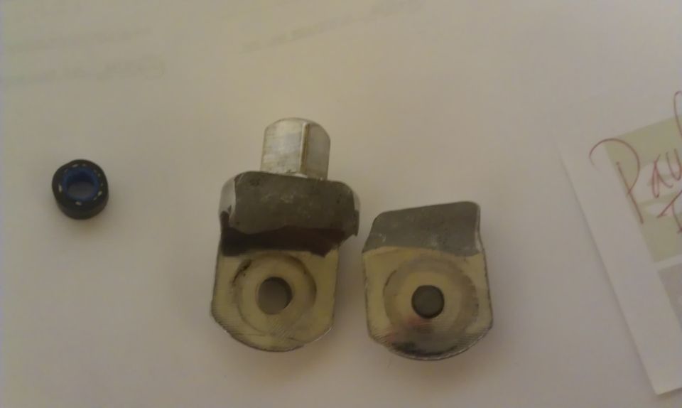 Two metal brackets and a small bearing on a white surface