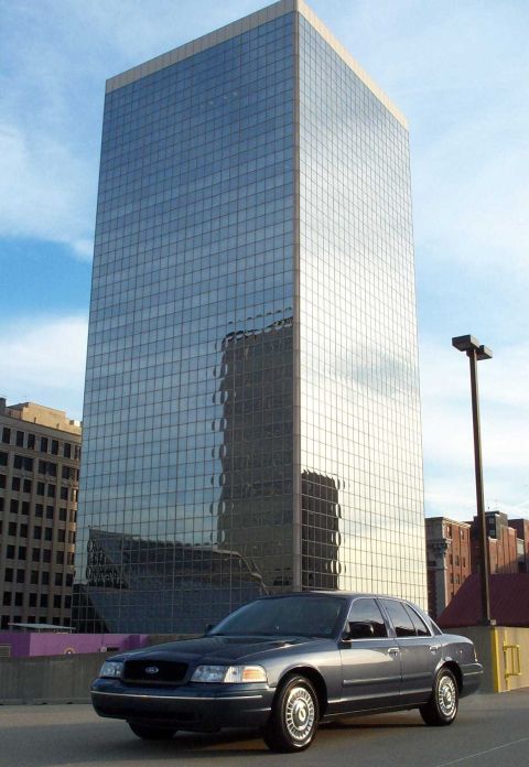 1998 Ford Crown Victoria - A dark sedan is parked in front of a modern glass building.