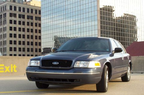 1998 Ford Crown Victoria - A dark blue 1998 Ford Crown Victoria is seen parked in front of reflective glass buildings.