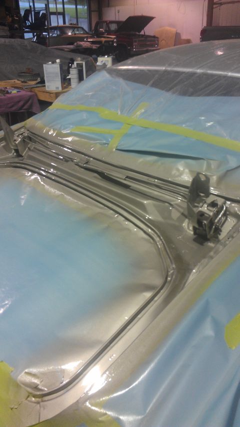 1973 Chevrolet Camaro - A car's hood and windshield area are covered in protective plastic sheeting and tape, with chrome trim visible.