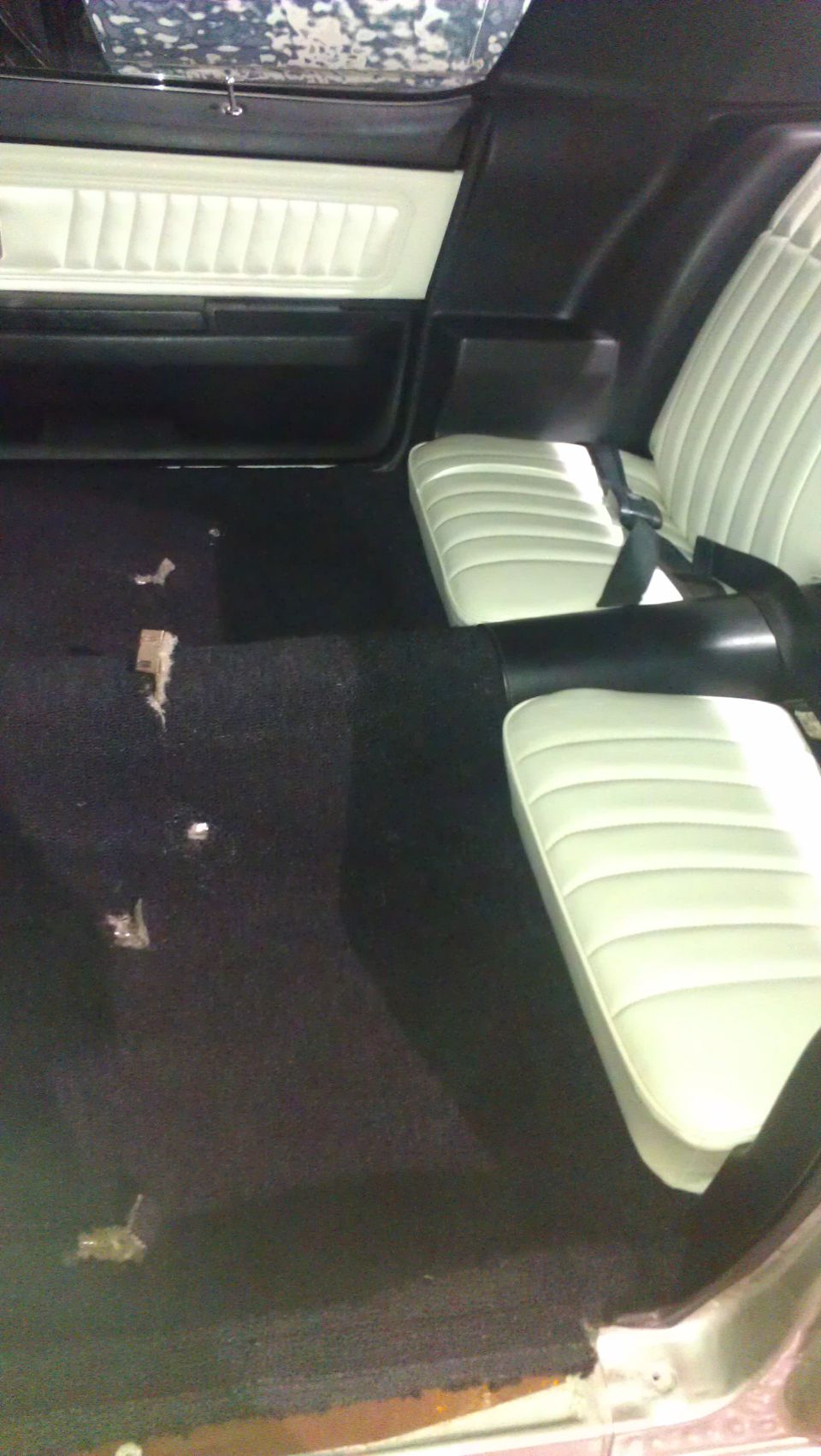 Interior shot of a car with black carpet and white seats. Door panel is visible