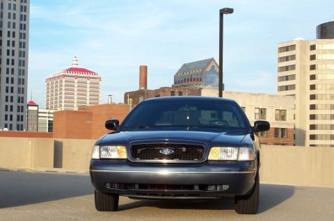 1998 Ford Crown Victoria - A dark blue sedan is parked on a rooftop with a cityscape behind it.