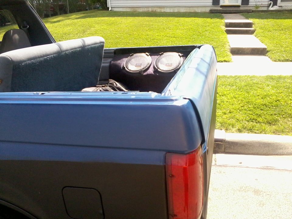 Rear interior of a blue Ford Bronco, showing the back seat and cargo area with two speakers mounted behind the seat