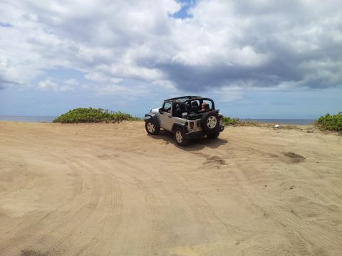 1990 Chevrolet Suburban - Jeep Wrangler parked on a sandy beach with the ocean in the distance under a cloudy sky.