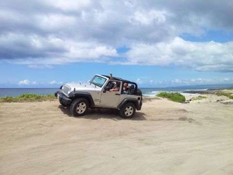 1990 Chevrolet Suburban - A silver Jeep Wrangler drives along a sandy coastline under a cloudy sky.