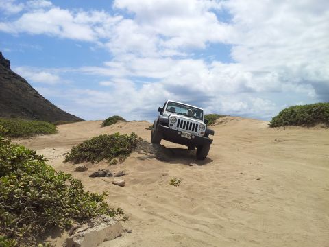 1990 Chevrolet Suburban - A white Jeep Wrangler navigates a sandy terrain under a cloudy sky.