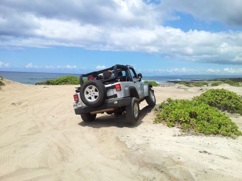 1990 Chevrolet Suburban - A silver Jeep Wrangler is parked on a sandy path near the ocean under a cloudy sky.
