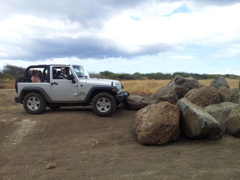 1990 Chevrolet Suburban - A silver Jeep Wrangler with its top removed is parked on a dirt path near a pile of large rocks under a cloudy sky.