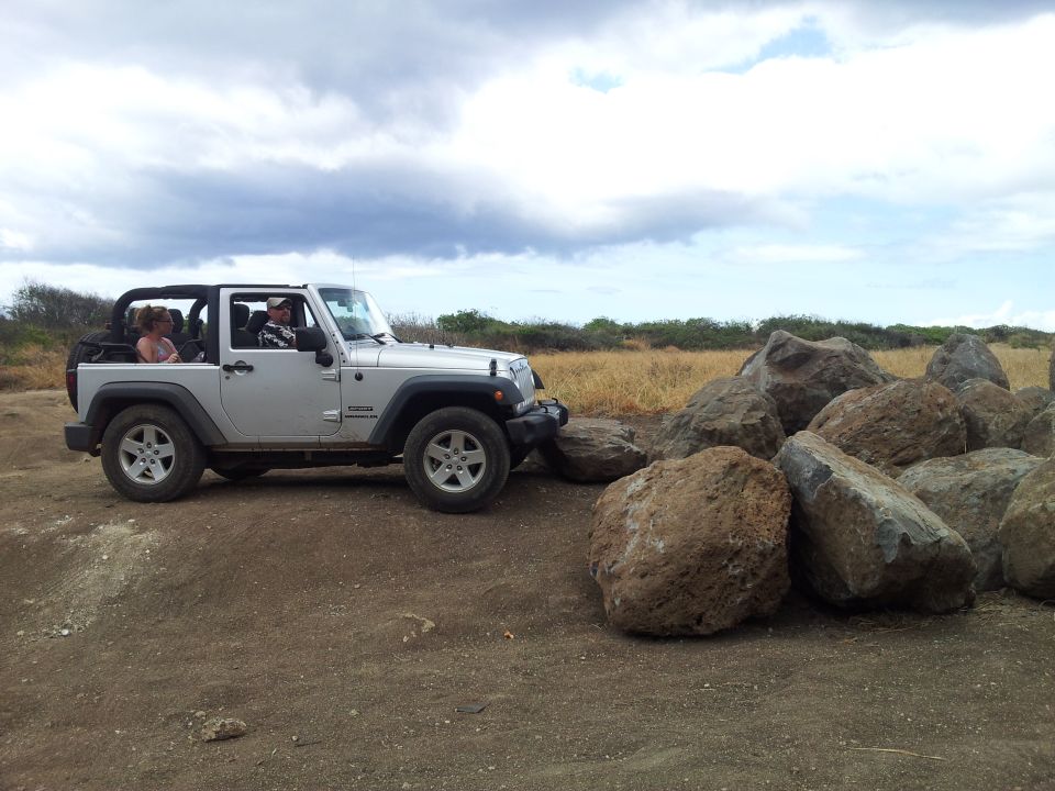 Silver Jeep Wrangler with people inside parked on a dirt road next to large rocks