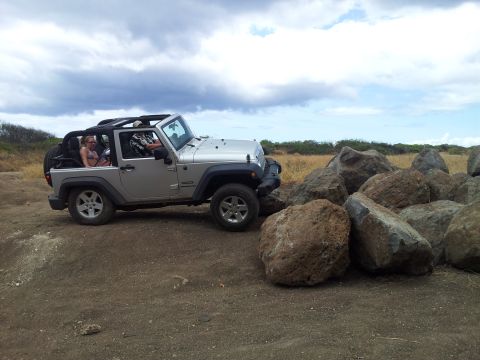 1990 Chevrolet Suburban - A silver Jeep Wrangler is parked on a dirt path next to a pile of large rocks under a cloudy sky.