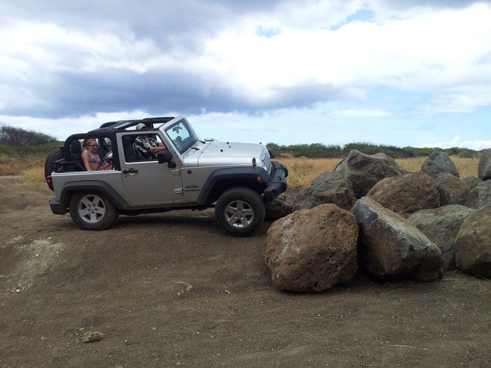 Silver Jeep Wrangler parked next to large rocks on a dirt path