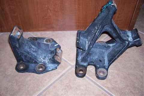 1986 Ford Bronco - Two black metal engine mounts are shown on a tiled floor against a wooden background.