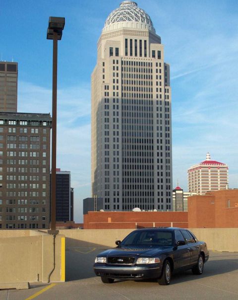 1998 Ford Crown Victoria - A dark sedan is parked on a rooftop with a prominent skyscraper and other buildings in the background.