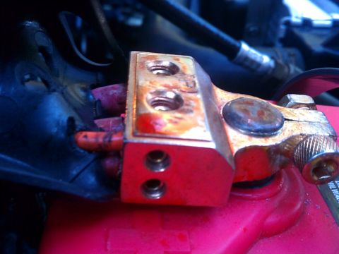1993 Ford Bronco - Close-up of a corroded car battery terminal with visible red plastic and a black cable.