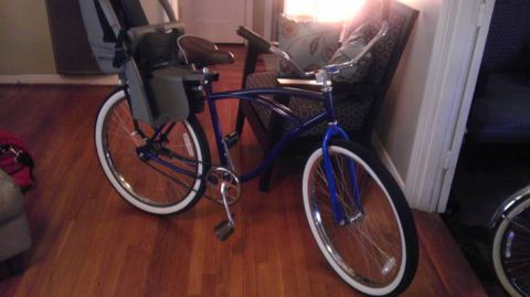 1953 Ford Mainline - A blue cruiser bicycle with whitewall tires and a child seat is parked indoors on a wooden floor.