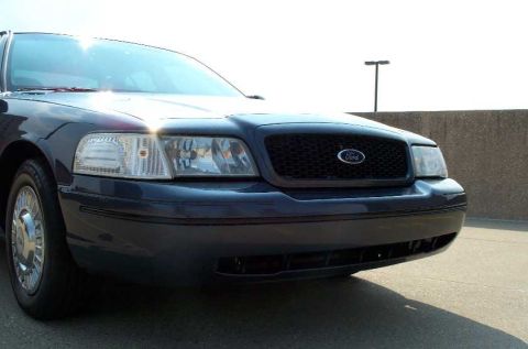 1998 Ford Crown Victoria - The front end of a dark blue Ford Crown Victoria is visible, showing the grille and headlights.