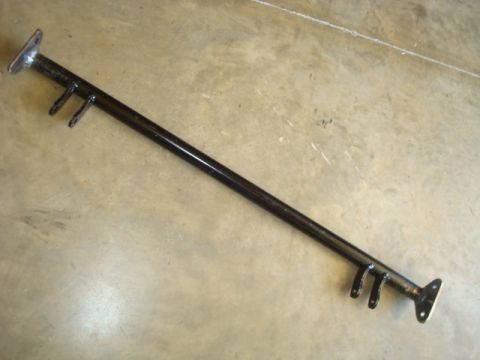 1995 Ford Bronco - A black metal bar with mounting flanges and brackets is shown on a concrete floor. The part appears to be a suspension component.