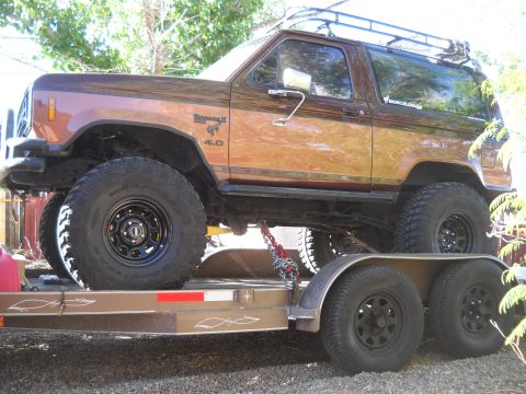 2012 Ford Mustang - A lifted Ford Bronco II is secured to a trailer with chains, ready for transport.