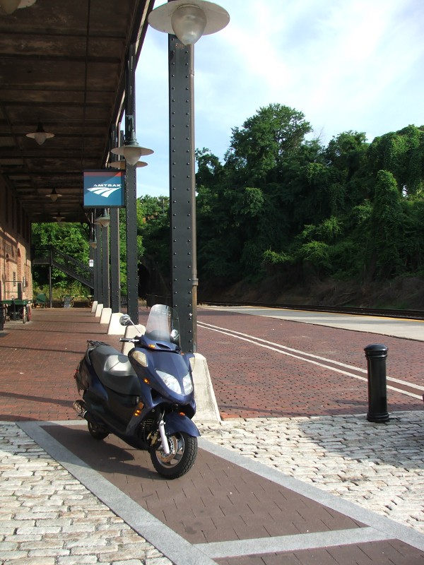 Blue scooter parked at train station platform with Amtrak sign