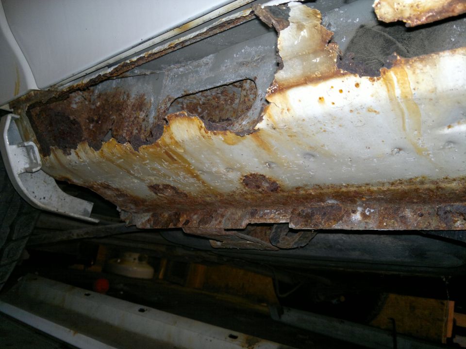 Close-up of a heavily rusted car rocker panel and undercarriage