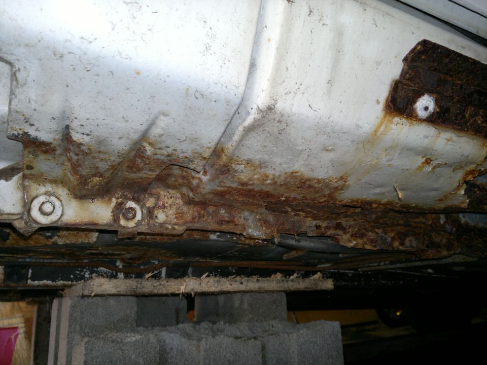 Undercarriage of a vehicle showing significant rust damage on the frame and body panels