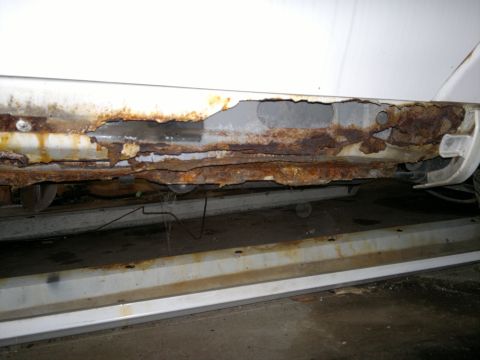 1993 Ford Taurus - The lower body panel of this vehicle is severely damaged by rust, with large sections missing.