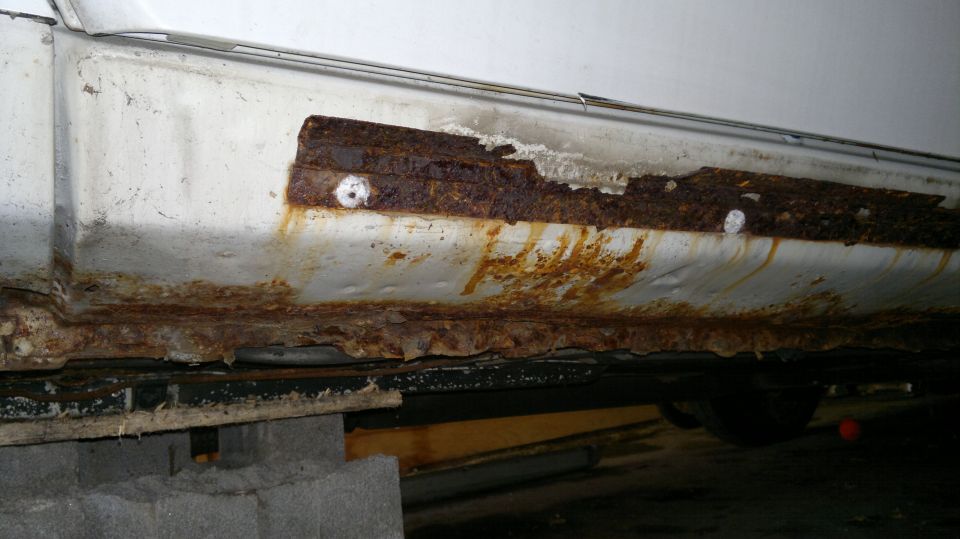Heavily rusted rocker panel on a white car, showing significant corrosion and damage
