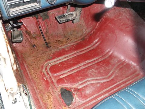 1971 Ford Ranchero - Vehicle interior floor shows significant rust and wear on the red carpet.