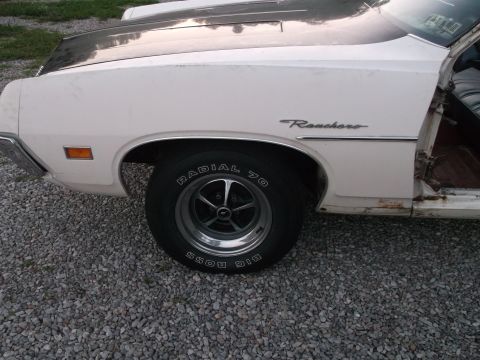 1971 Ford Ranchero - A white Ford Ranchero with a black hood stripe is seen from the side, revealing its interior and rusted lower body panels.