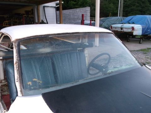 1971 Ford Ranchero - Interior view of a white vehicle with blue seats and a black steering wheel, with another vehicle covered in a blue tarp in the background.