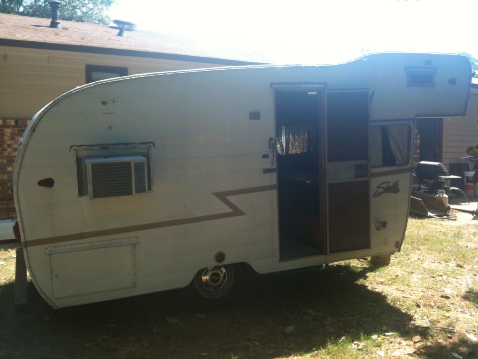 White travel trailer with brown zigzag stripe and an air conditioner unit, parked outdoors