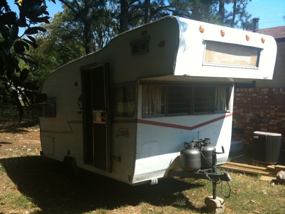 White travel trailer with red stripe, two propane tanks on hitch, parked outdoors